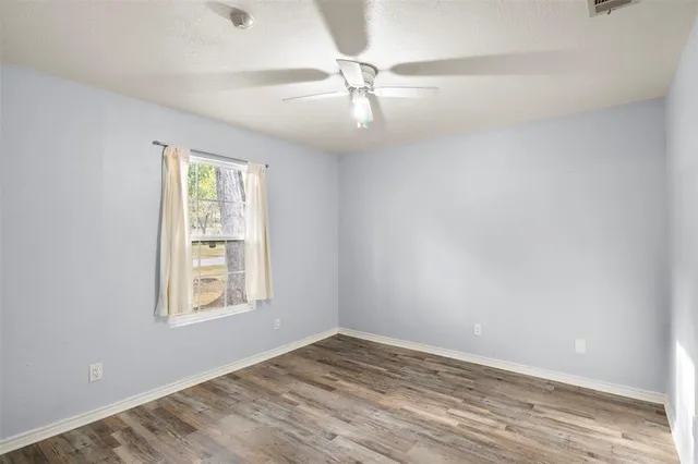 an empty room with wooden floor windows and fan