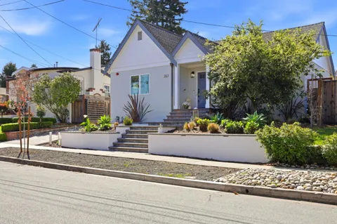 a front view of a house with lots of flowers and trees