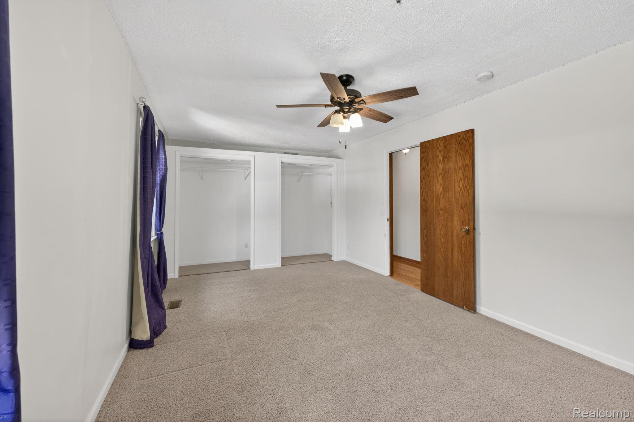 9353 Hill Road Swartz Creek, MI 48473 - Photo 39 of 98 Spacious room featuring neutral carpeting, white walls, two open closet spaces, a ceiling fan with integrated lighting, and a wood-finish door