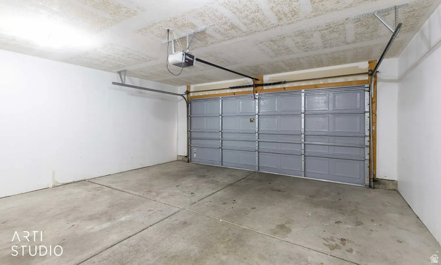 Concrete flooring with visible expansion joints, white painted walls, and a paneled garage door