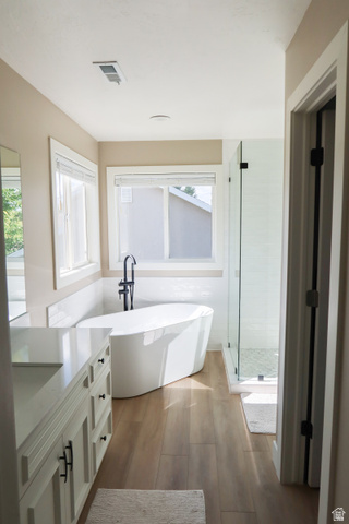 1204 North 3020th Street West Provo, UT 84601 - Photo 28 of 35 Freestanding soaking tub with a floor-mounted faucet, glass-enclosed shower, white vanity with an integrated sink, wood-finish flooring, and crisp white trim