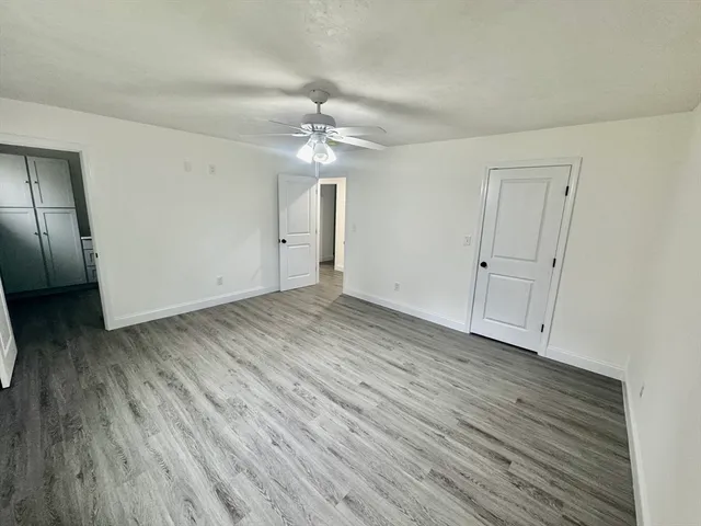 an empty room with wooden floor chandelier fan and refrigerator
