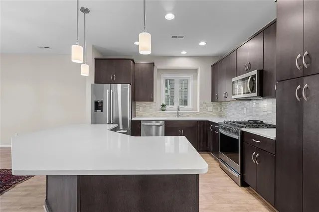 a large kitchen with stainless steel appliances kitchen island granite countertop a refrigerator a sink dishwasher a stove and white cabinets with wooden floor