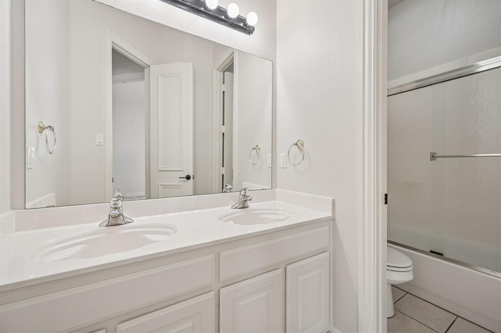 3309 Ricci Lane Irving, TX 75062 - Photo 24 of 36 Full bath with double vanity, light tile patterned floors, and enclosed tub / shower combo