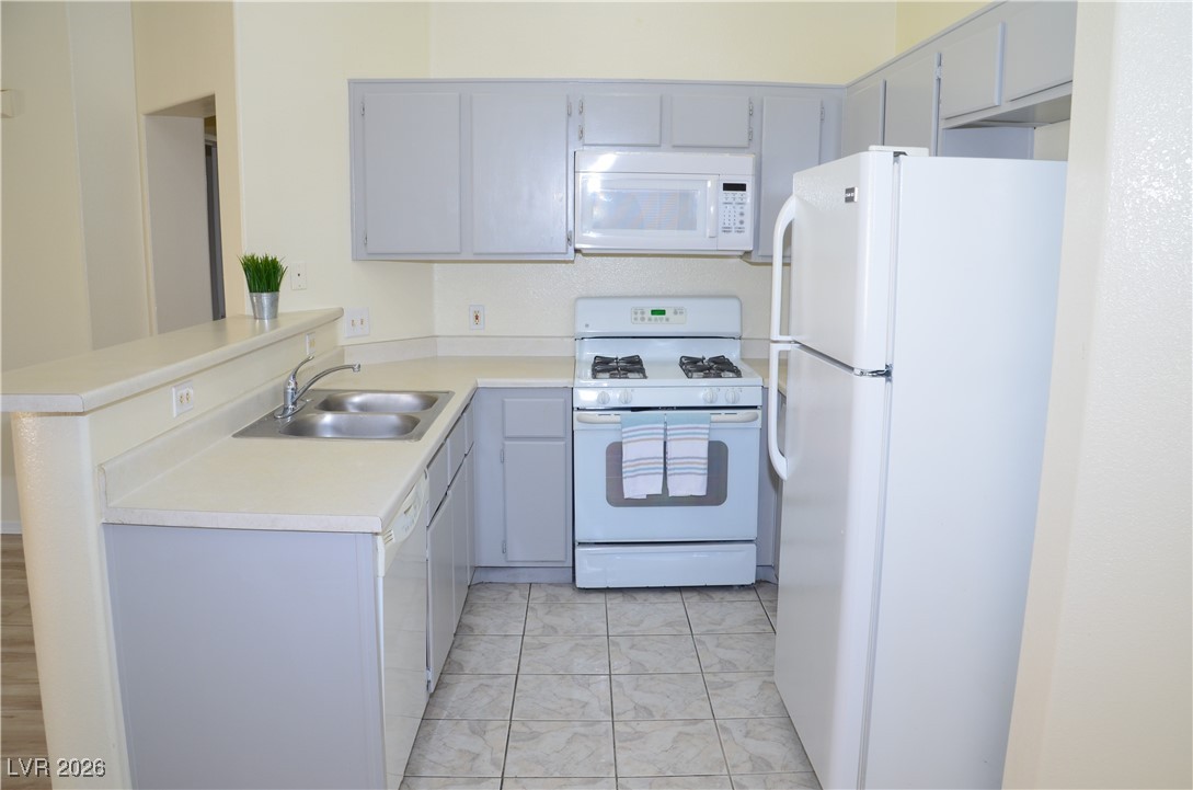 1881 West Alexander Road, Unit 2101 North Las Vegas, NV 89032 - Photo 5 of 37 Kitchen with a peninsula, white appliances, gray cabinets, and light countertops