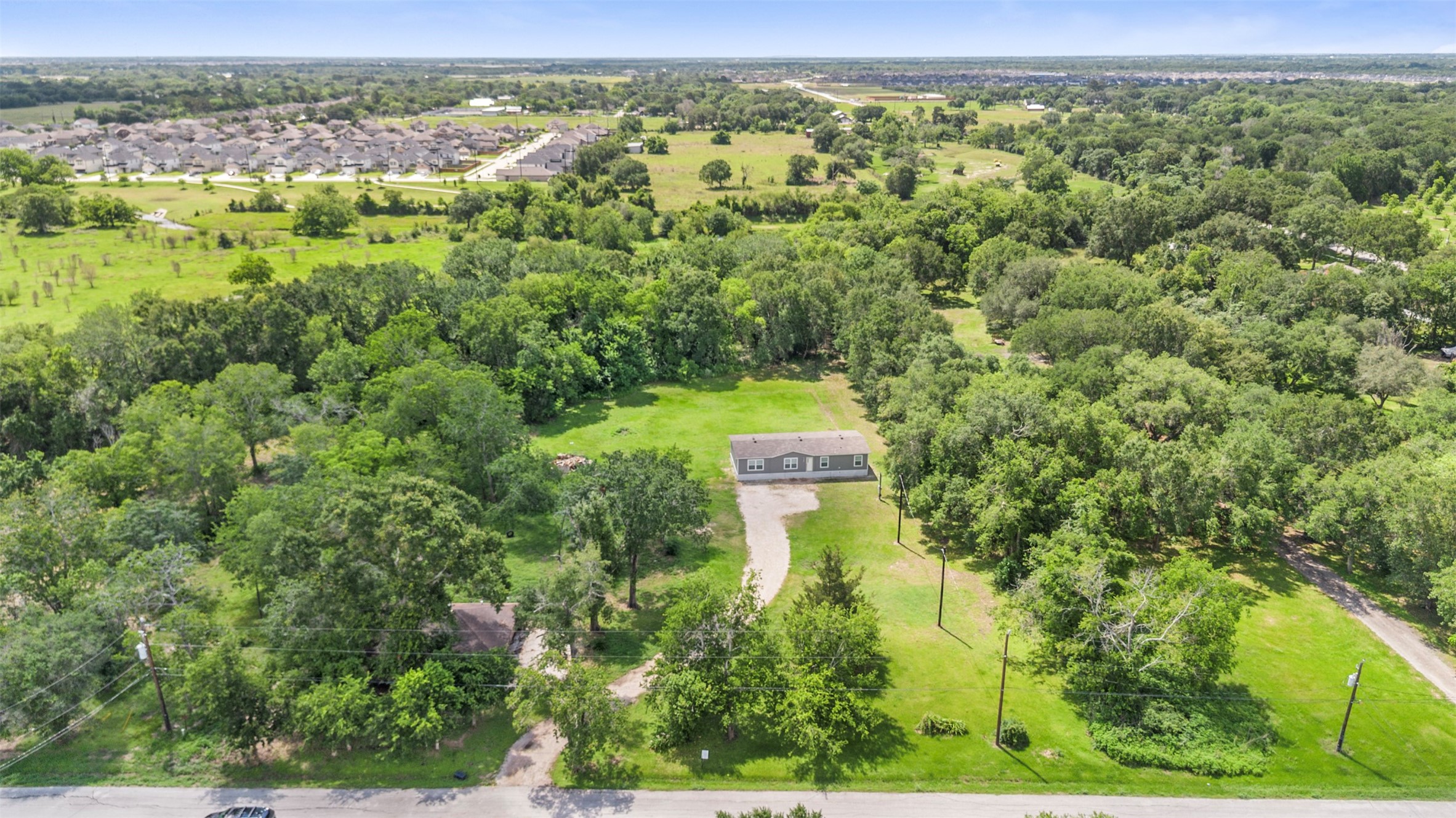 2701 Mazen Road Rosenberg, TX 77471 - Photo 2 of 10 This photo showcases a spacious property surrounded by lush greenery, offering privacy and tranquility. The house sits centrally on a large plot, with ample open space and mature trees. Nearby, a residential neighborhood is visible, providing a sense of community while maintaining a peaceful setting.