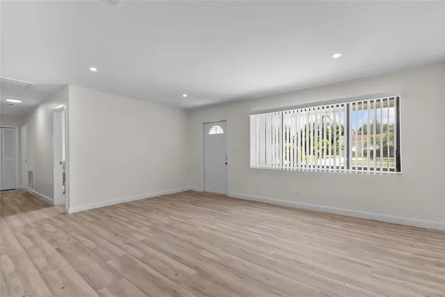 a view of an empty room with wooden floor and a window