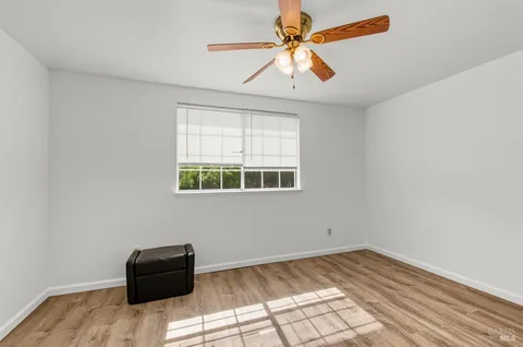 an empty room with wooden floor fan and windows