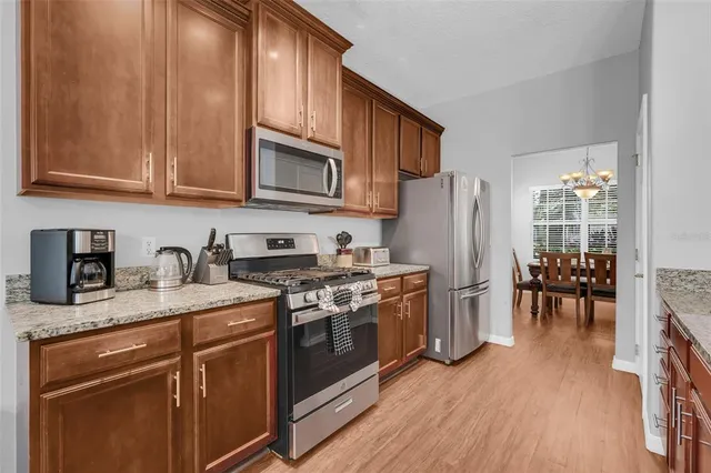 a kitchen with stainless steel appliances granite countertop wooden cabinets a refrigerator a stove a sink and a dining table with wooden floor