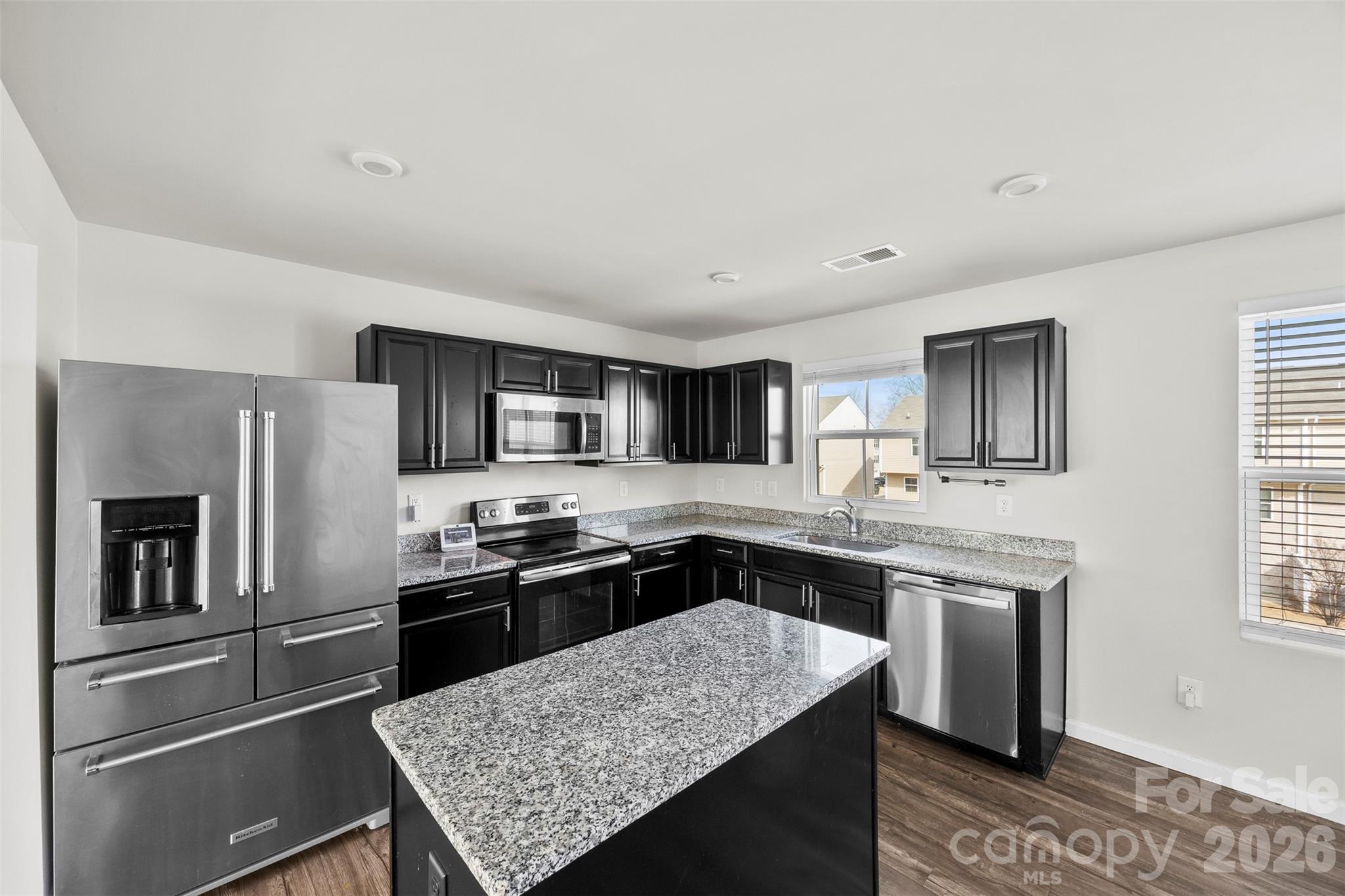 a kitchen with stainless steel appliances granite countertop a stove a sink dishwasher a refrigerator and white cabinets with wooden floor