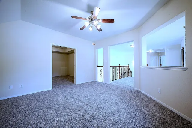 an empty room with chandelier fan and a kitchen view