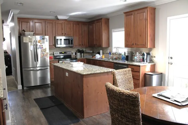 a kitchen with stainless steel appliances granite countertop a refrigerator a stove a sink a dining table and chairs