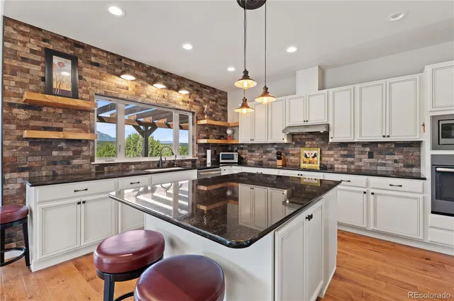 a kitchen with stainless steel appliances granite countertop a sink a stove a refrigerator and white cabinets with wooden floor