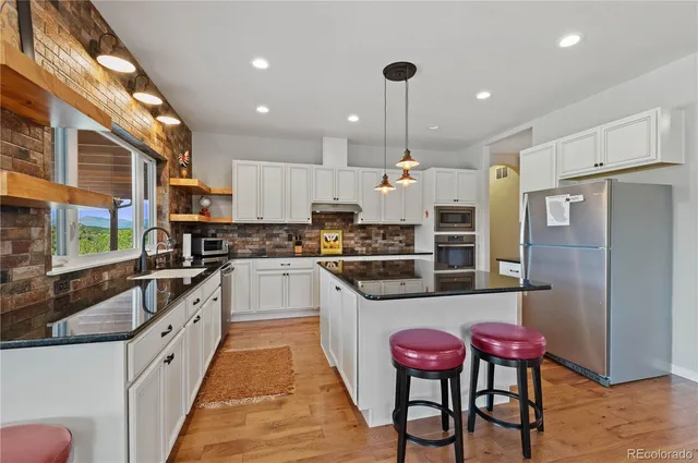 a large kitchen with stainless steel appliances kitchen island granite countertop a table chairs and a refrigerator