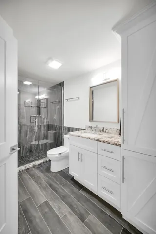 a bathroom with a granite countertop sink a toilet a mirror and shower