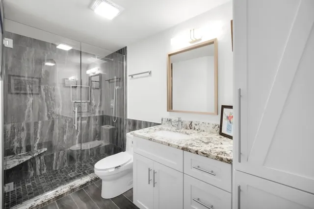 a bathroom with a granite countertop sink toilet a mirror and shower
