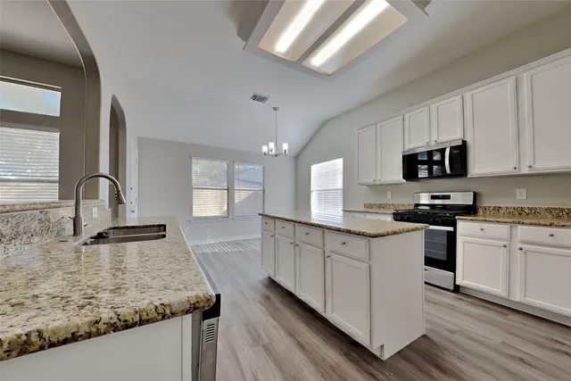 a kitchen with granite countertop a sink stainless steel appliances and white cabinets