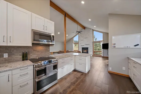 a kitchen with stainless steel appliances granite countertop a stove top oven a sink a refrigerator white cabinets and wooden floor