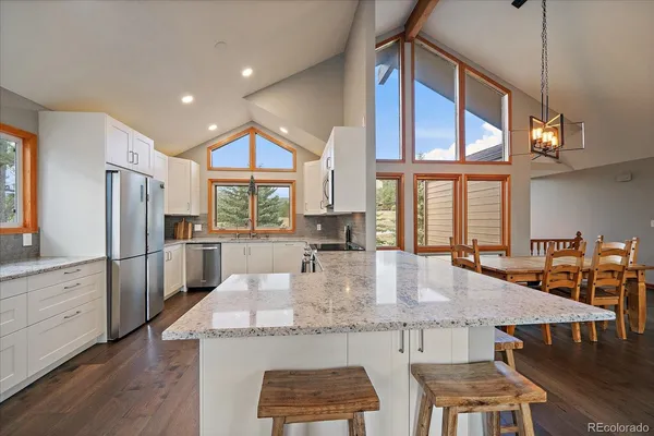 a kitchen with stainless steel appliances granite countertop a stove a refrigerator a kitchen island a table and chairs