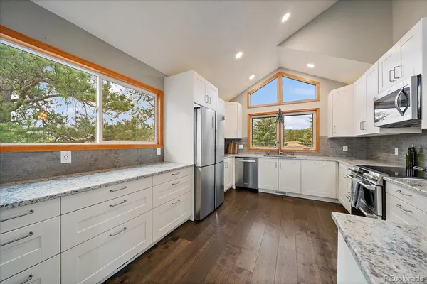 a kitchen with granite countertop white cabinets a sink a window and stainless steel appliances
