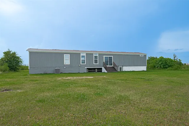 a view of a lake in a big yard with lawn chairs and large trees