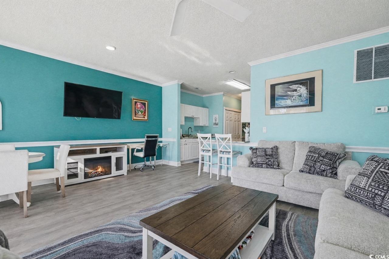 1512 Lanterns Rest Road, Unit 102 Myrtle Beach, SC 29579 - Photo 4 of 21 Living room with wood finished floors, crown molding, a desk, a textured ceiling, and a glass covered fireplace