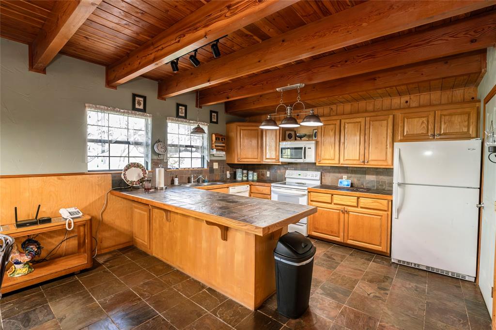 698 Storey Road Nocona, TX 76255 - Photo 24 of 34 Kitchen with white appliances, pendant lighting, a wood ceiling with exposed beams, brown cabinetry, and a peninsula