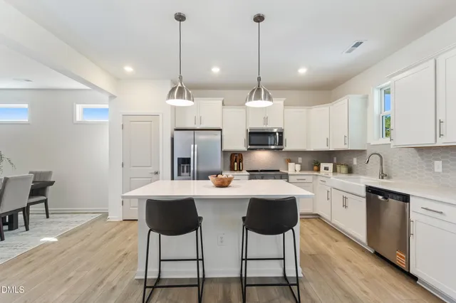 a kitchen with stainless steel appliances kitchen island a white table chairs and a refrigerator