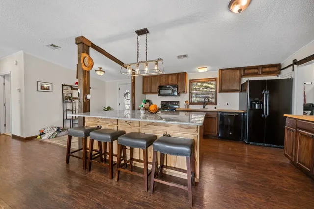 a kitchen with stainless steel appliances kitchen island granite countertop a table chairs and a refrigerator