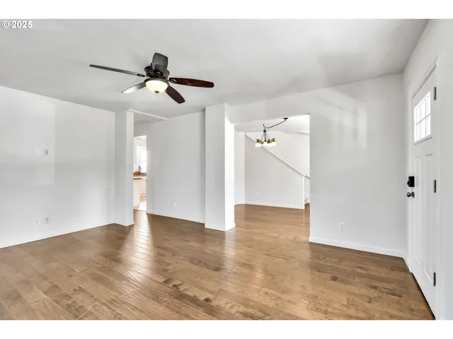 a view of an empty room with wooden floor and a ceiling fan