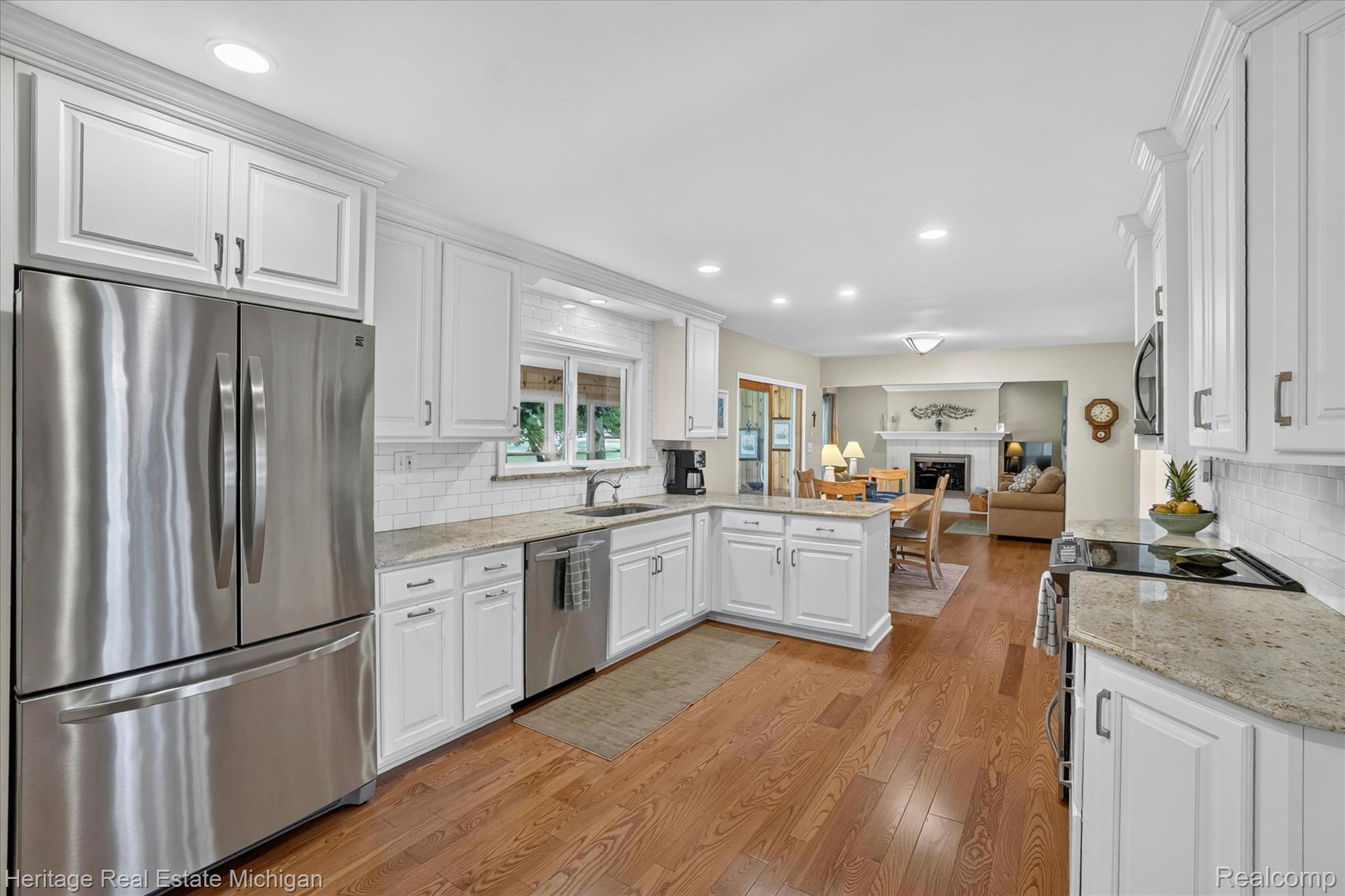 14038 North Hogan Road Linden, MI 48451 - Photo 20 of 53 Modern kitchen featuring white shaker cabinetry, stainless steel appliances, granite countertops, subway tile backsplash, and wood-finish flooring