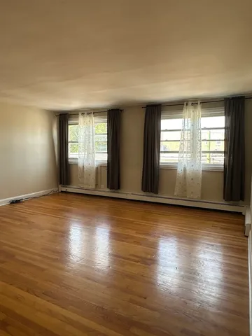 an empty room with wooden floor and windows with curtains