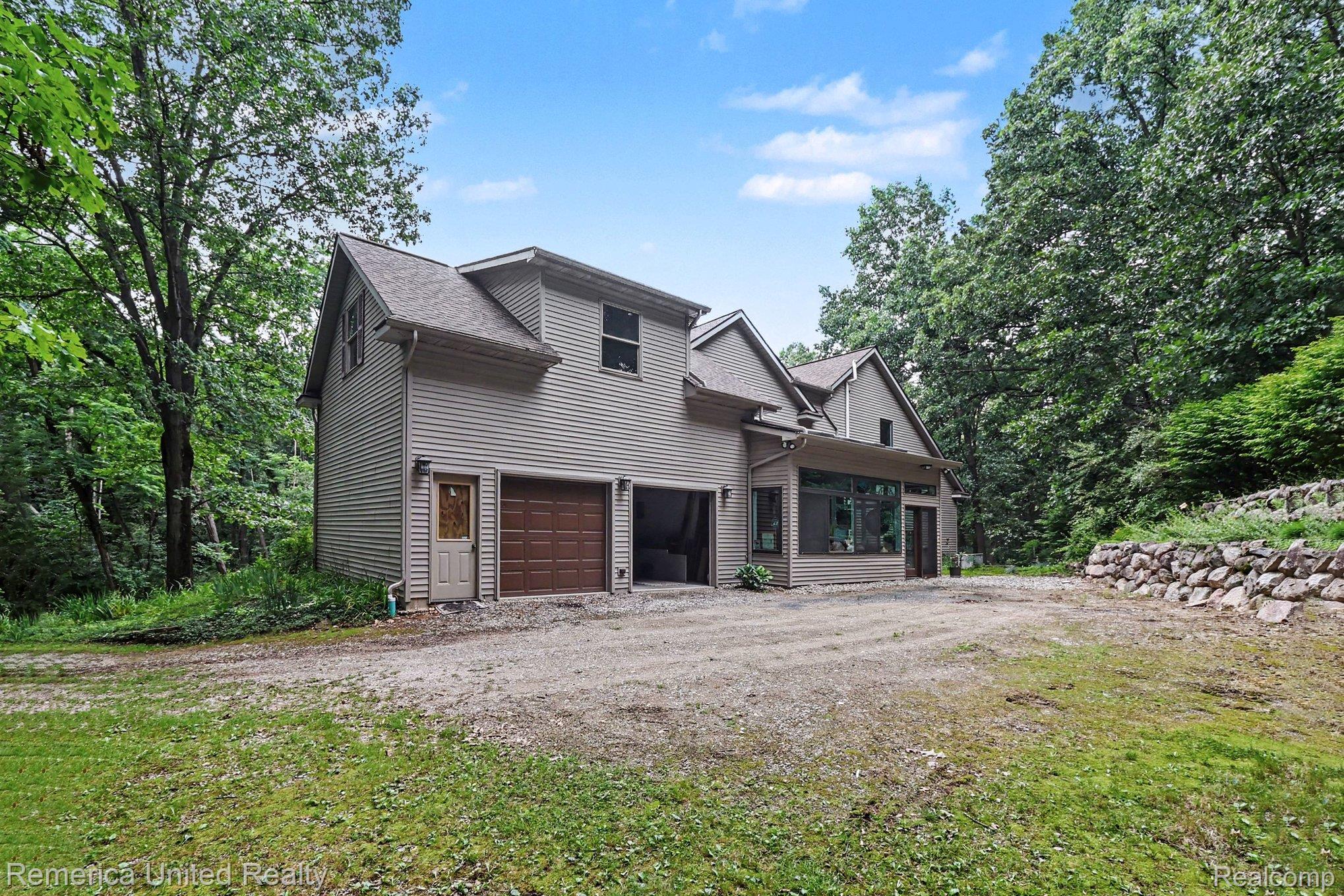 20962 Wasson Road Gregory, MI 48137 - Photo 34 of 39 Contemporary home exterior featuring neutral-toned siding, a two-car garage with brown doors, an additional entry door, and large windows