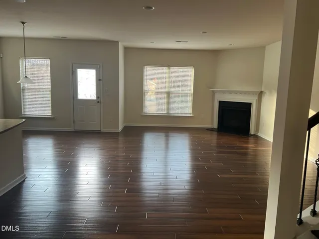 an empty room with wooden floor fireplace and windows