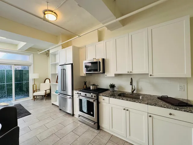 a kitchen with stainless steel appliances granite countertop a refrigerator a stove a sink and a white wooden cabinets