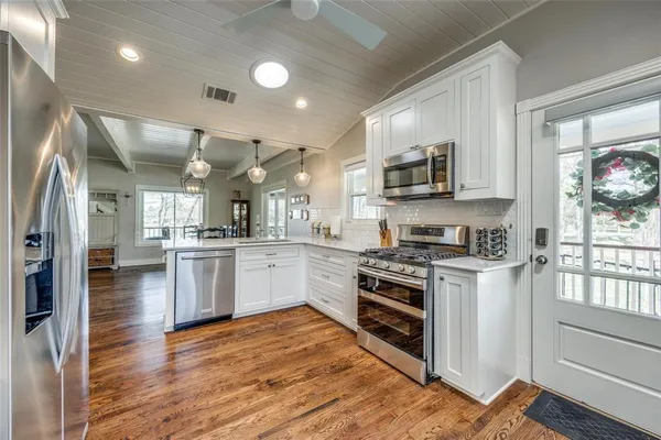 a kitchen with stainless steel appliances granite countertop a stove top oven a sink dishwasher and a refrigerator with wooden floor