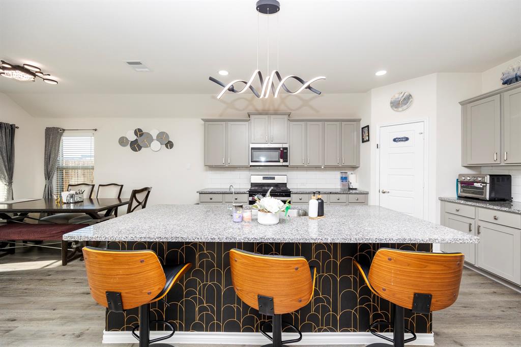 3229 Trails End Road Aubrey, TX 76227 - Photo 15 of 25 Kitchen featuring gray cabinetry, decorative backsplash, a kitchen breakfast bar, light stone countertops, and recessed lighting