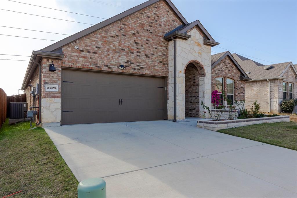 3229 Trails End Road Aubrey, TX 76227 - Photo 4 of 25 French country home featuring stone siding, concrete driveway, a front lawn, and an attached garage