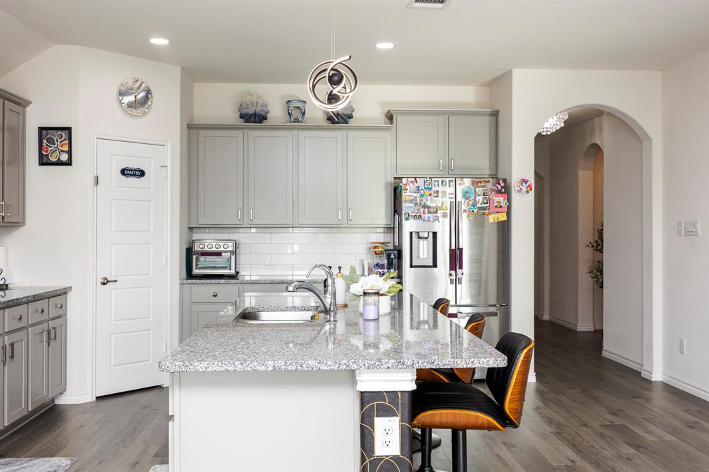 3229 Trails End Road Aubrey, TX 76227 - Photo 6 of 25 Kitchen with gray cabinetry, stainless steel fridge with ice dispenser, a breakfast bar area, and light stone countertops
