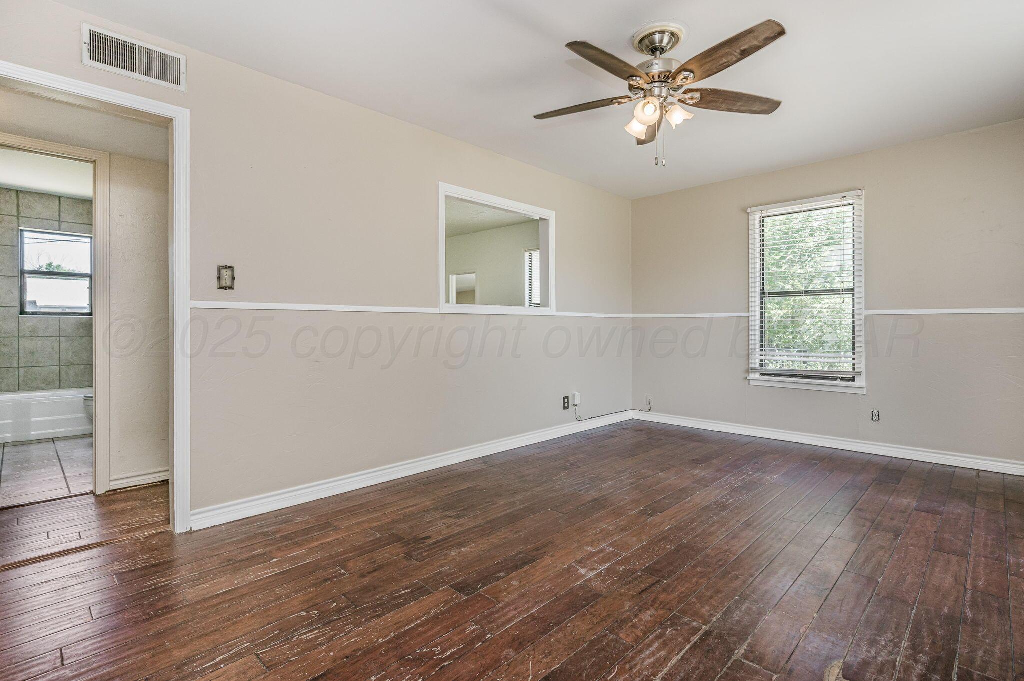4004 South Van Buren Street Amarillo, TX 79110 - Photo 3 of 17 an empty room with wooden floor chandelier fan and windows