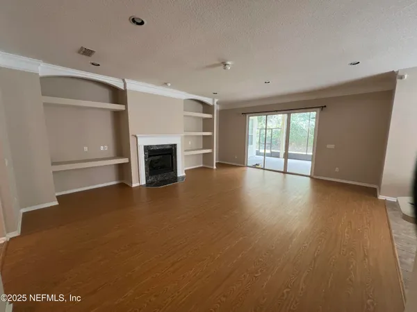 an empty room with wooden floor fireplace and windows