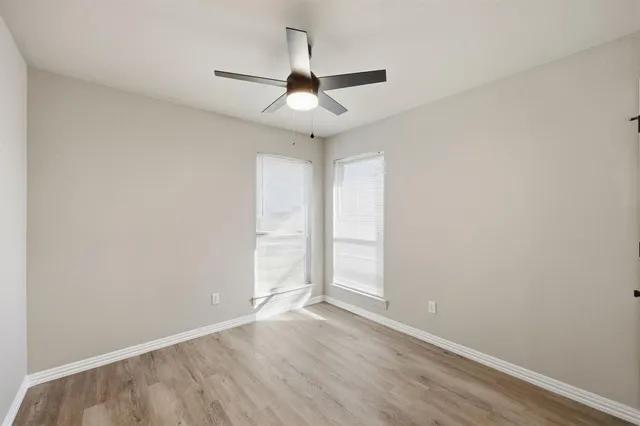 an empty room with wooden floor ceiling fan and window