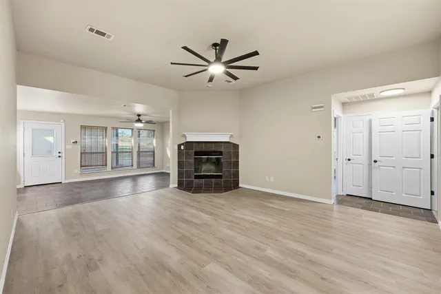 an empty room with wooden floor chandelier fan and windows