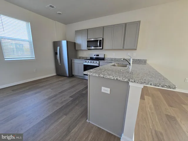 a kitchen with granite countertop a refrigerator a stove a sink and dishwasher with wooden floors