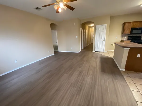 a view of an empty room with wooden floor and a ceiling fan