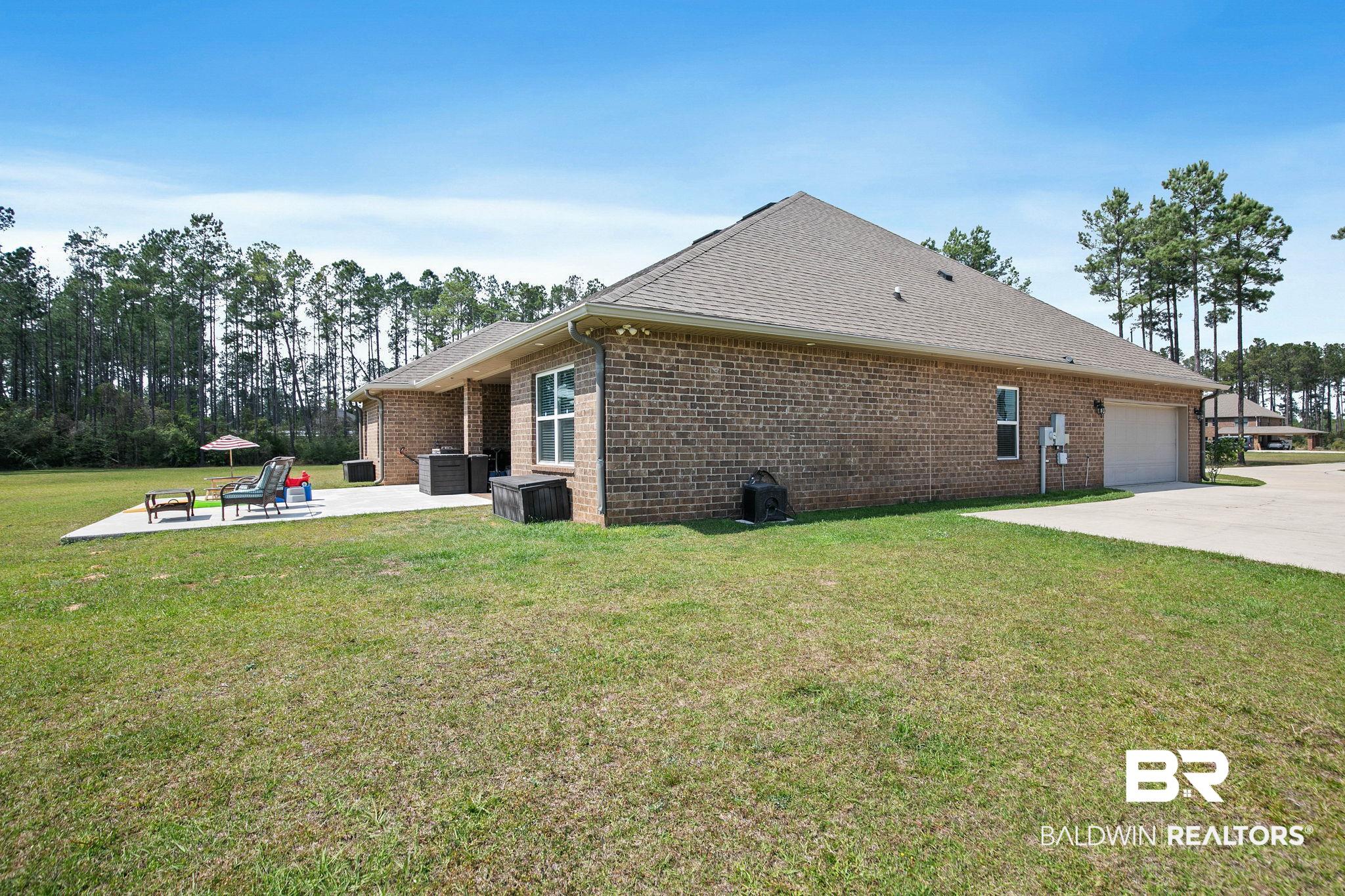 12750 B Jenkins Pit Road Daphne, AL 36527 - Photo 61 of 89 View of home's exterior featuring a yard, brick siding, an attached garage, a patio, and roof with shingles