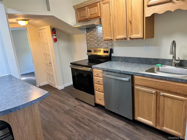 a kitchen with stainless steel appliances granite countertop a sink a stove a refrigerator a washer and dryer with wooden floors