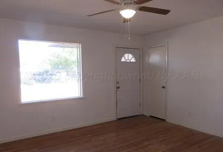 an empty room with wooden floor fan and windows