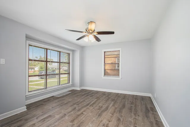 an empty room with chandelier fan and windows