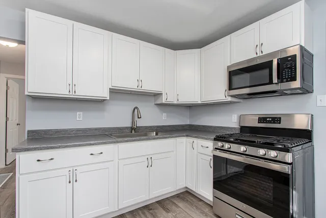 a kitchen with stainless steel appliances granite countertop grey cabinets a stove a sink and dishwasher